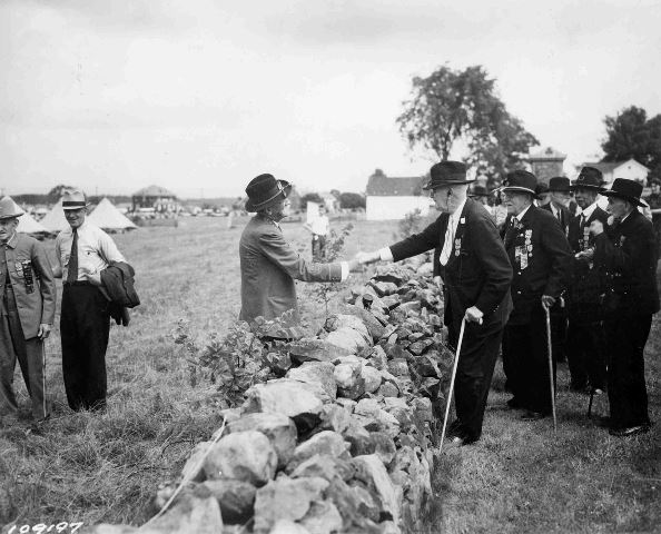 In what’s become an iconic photo representative of the 1913 Reunion, a Union and a Confederate veteran join hands across the stone wall at the High Water mark. Photo Courtesy: Adams County Historical Society.